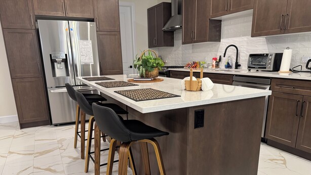 Uma cozinha moderna com uma ilha central, banquetas, geladeira e micro-ondas.