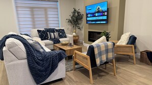 Uma sala de estar com sofá, duas poltronas, mesa de centro, televisão fixada na parede e lareira.