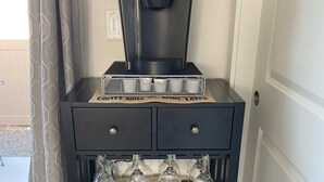 En svart kaffebryggare står på ett skåp, och under skåpet finns ett vinställ.