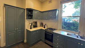 Une cuisine avec des meubles de couleur bleu foncé, une cuisinière à gaz, un évier et une fenêtre donnant sur l’extérieur.