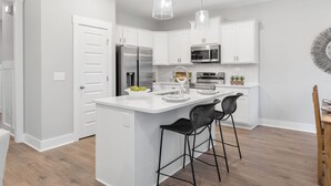 Une cuisine moderne avec des meubles blancs, des appareils en acier inoxydable et un îlot central doté de tabourets de bar.