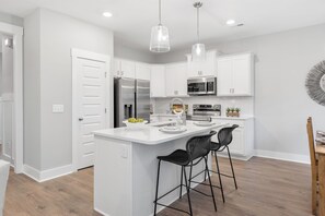 Een moderne keuken met witte kasten, roestvrijstalen apparatuur en een centraal eiland met barstoelen.