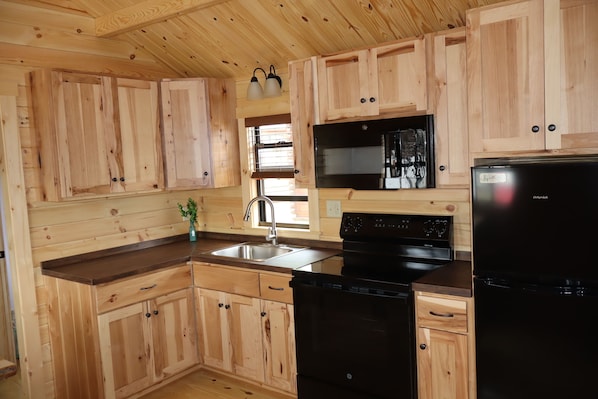 Una cocina con armarios de madera, un lavamanos de acero inoxidable, un lavavajillas negro y un refrigerador negro.