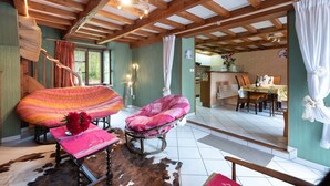 Un intérieur rustique avec des poutres apparentes, un coin repas avec une table et des chaises, et un espace salon confortable avec un canapé à motifs et un tapis en peau de vache.