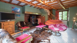 Un intérieur rustique avec une cheminée, des poutres en bois, un téléviseur et un chien.