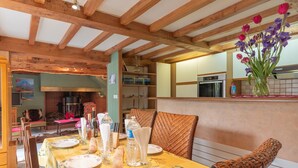 Un coin repas avec un plafond en bois, une table dressée pour deux personnes et un vase rempli de fleurs accroché au mur.