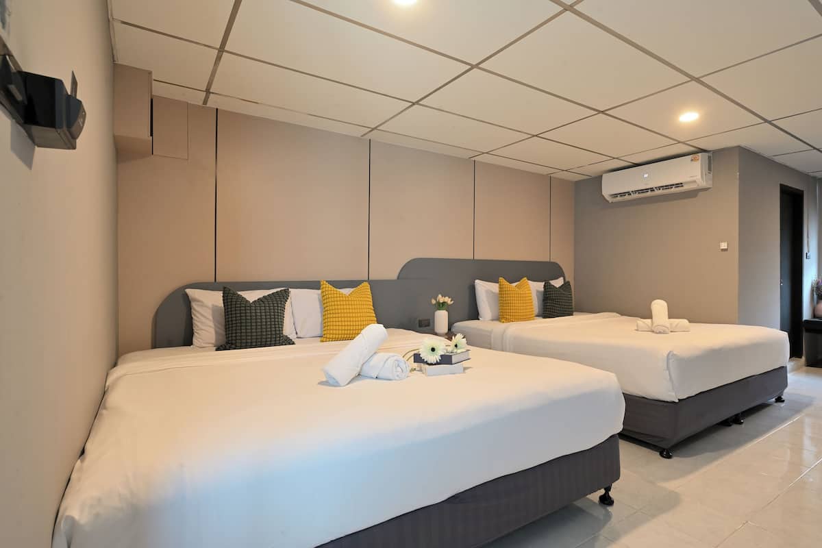 A hotel room with two beds, beige walls, and an air conditioning unit.