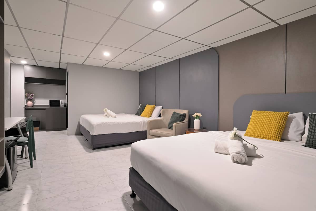 A modern hotel room with two beds, a desk, and a small kitchenette.