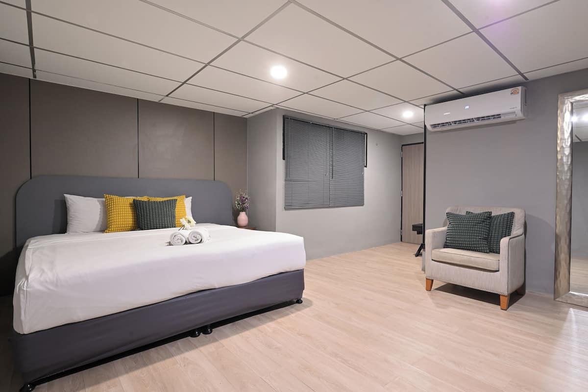 A modern bedroom with a large bed, a grey sofa, and a window with blinds.