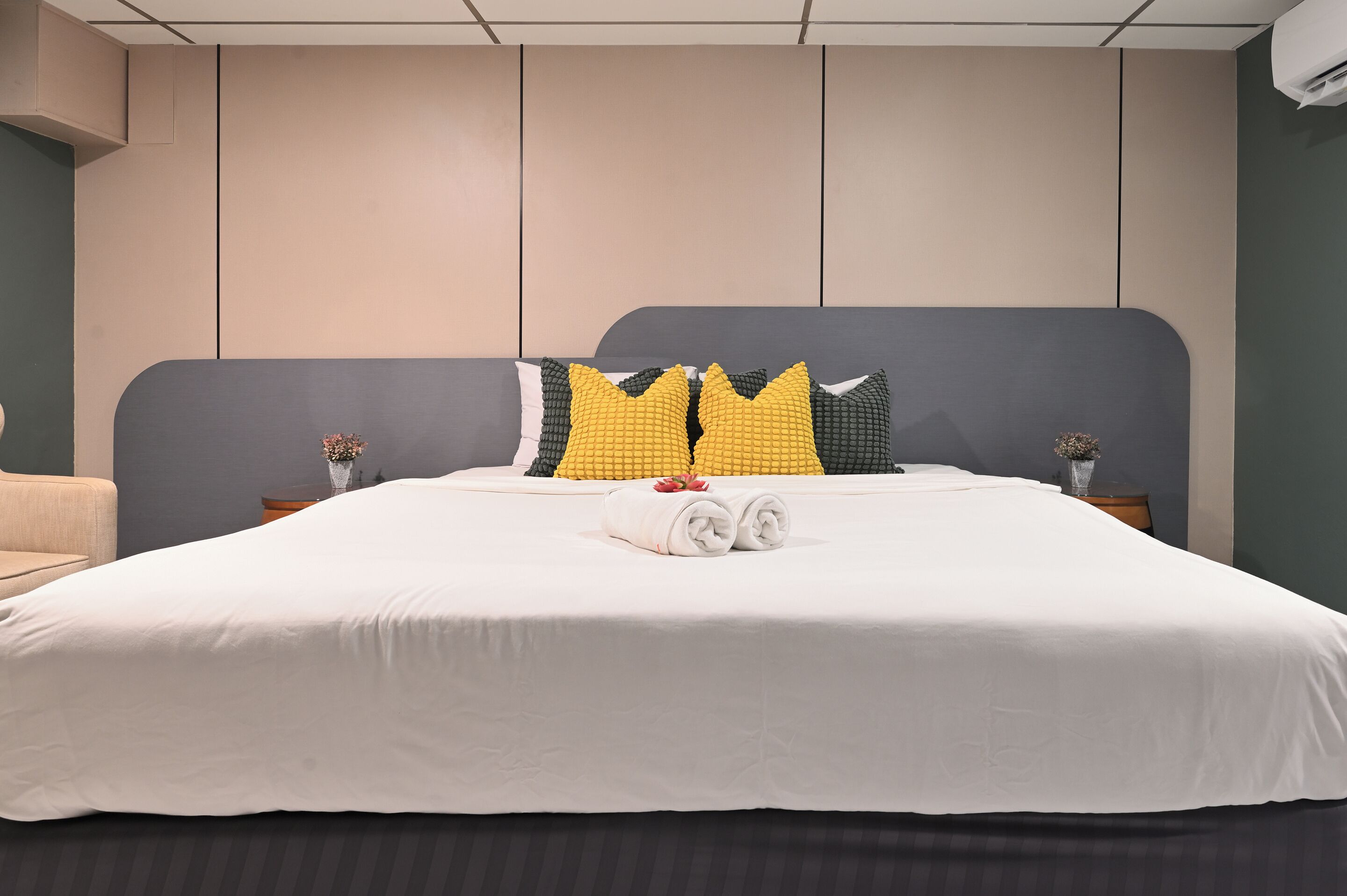 A neatly made bed with white bedding, a grey headboard, and decorative pillows in yellow and black.