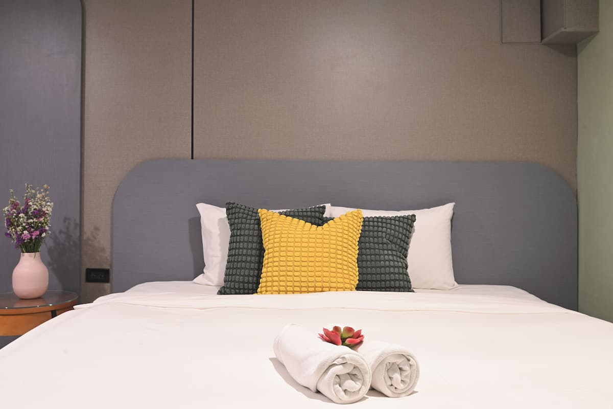 A neatly made bed with a white duvet, two rolled towels, and a small flower arrangement on the nightstand.
