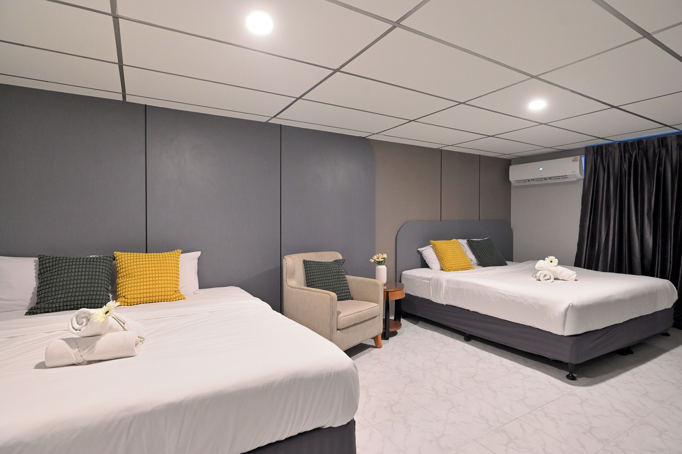 Habitación de hotel con dos camas, una silla, una mesita pequeña y un aire acondicionado.