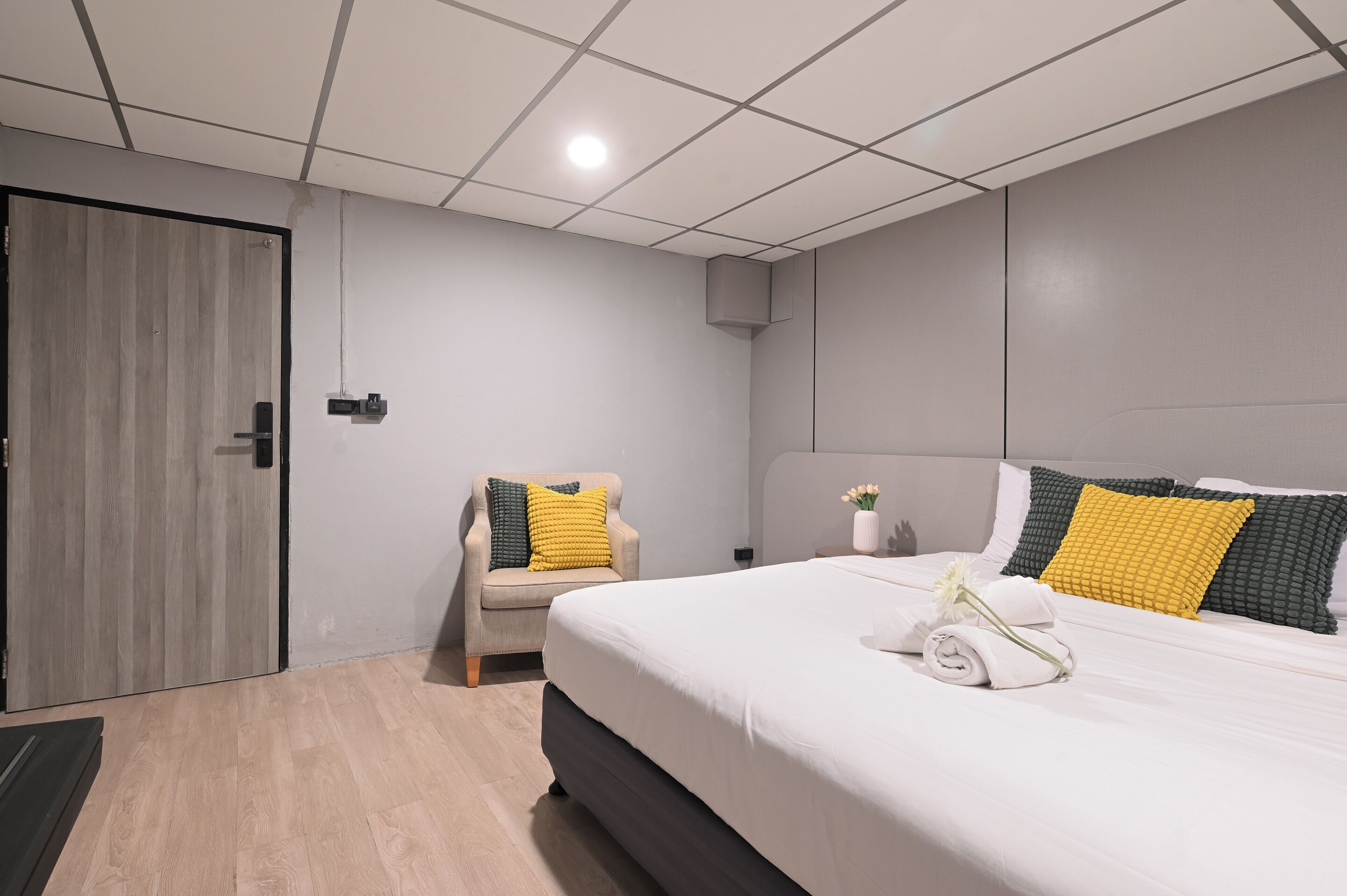 A modern hotel room with a large bed, a chair, a bedside table, and a door.