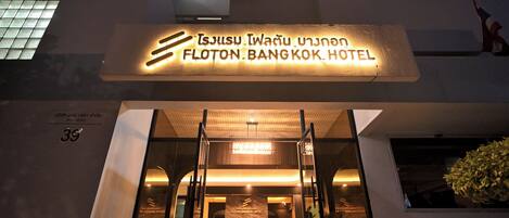 The exterior of the Flotton Bangkok Hotel with a modern design, illuminated sign, and entrance with glass doors.