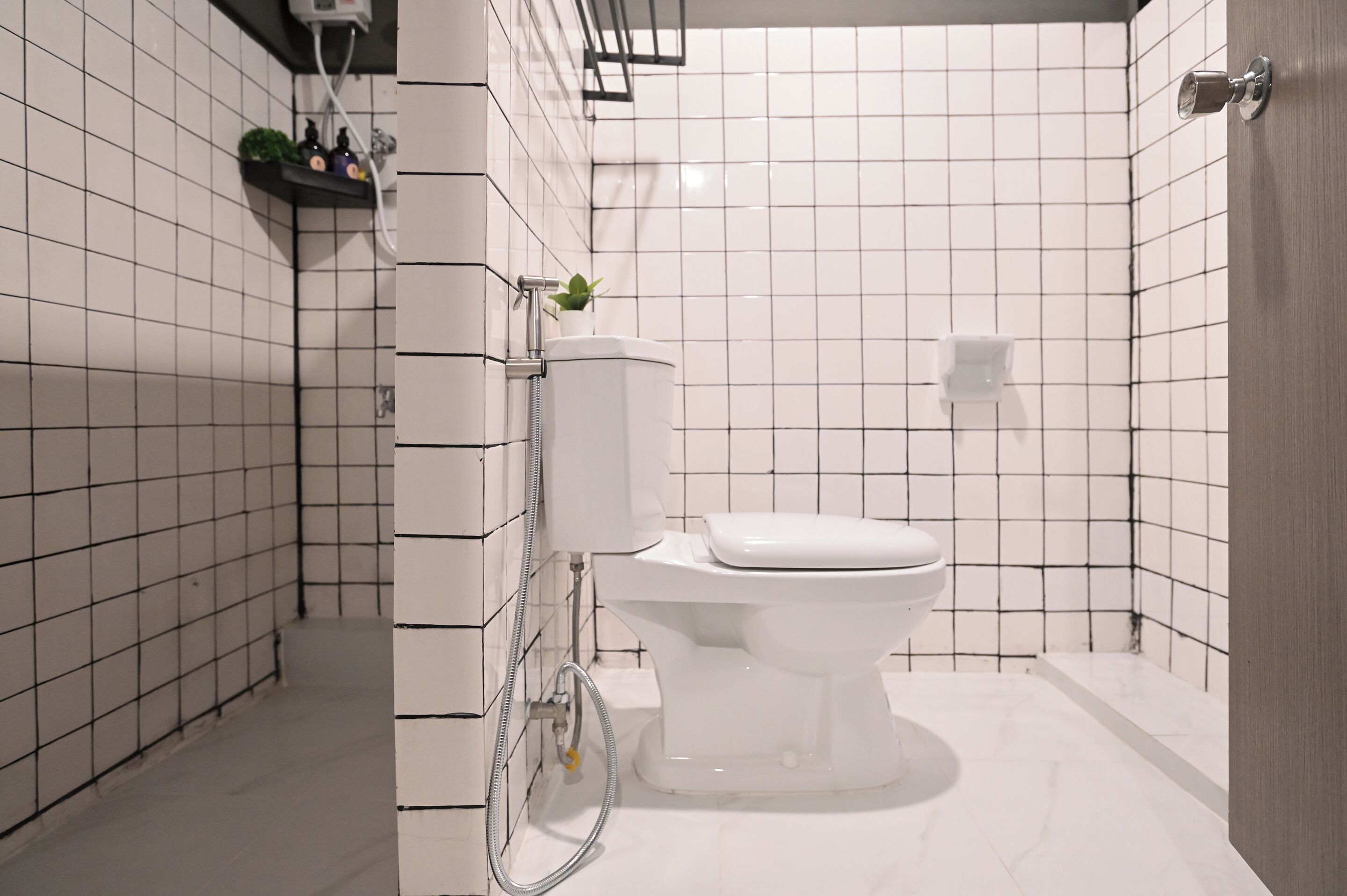 A modern bathroom with white tiled walls, a white toilet, a shower area, and a small shelf with toiletries.