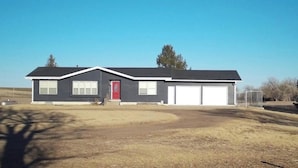 Una casa de dos pisos con puerta roja, garaje y un patio amplio.