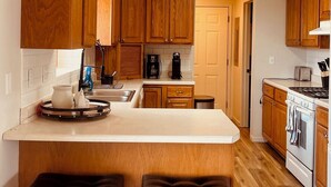 Una cocina compacta con armarios de madera, una isla central con taburetes, una estufa y una cafetera.