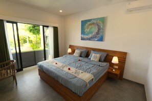 Een slaapkamer met een groot bed, twee nachtkastjes met lampen, een houten hoofdbord, een schilderij aan de muur en een glazen schuifdeur naar een balkon.