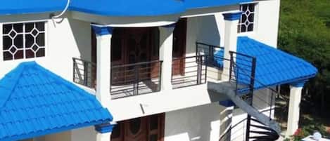 Un edificio de dos pisos con techo de tejas rojas, toldos azules y una escalera caracol.
