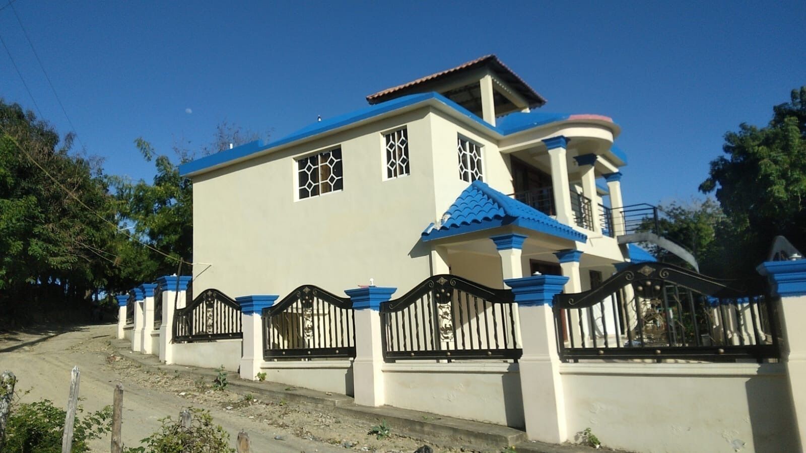 A two-story house with a blue roof, white walls, and black gates.