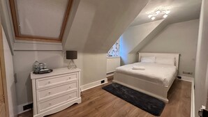 Una camera da letto con soffitto spiovente, un letto, una cassettiera, un termosifone e una finestra con vista.