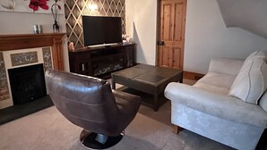 Un soggiorno con camino, televisione, una poltrona in pelle marrone, un divano bianco e una porta in legno.