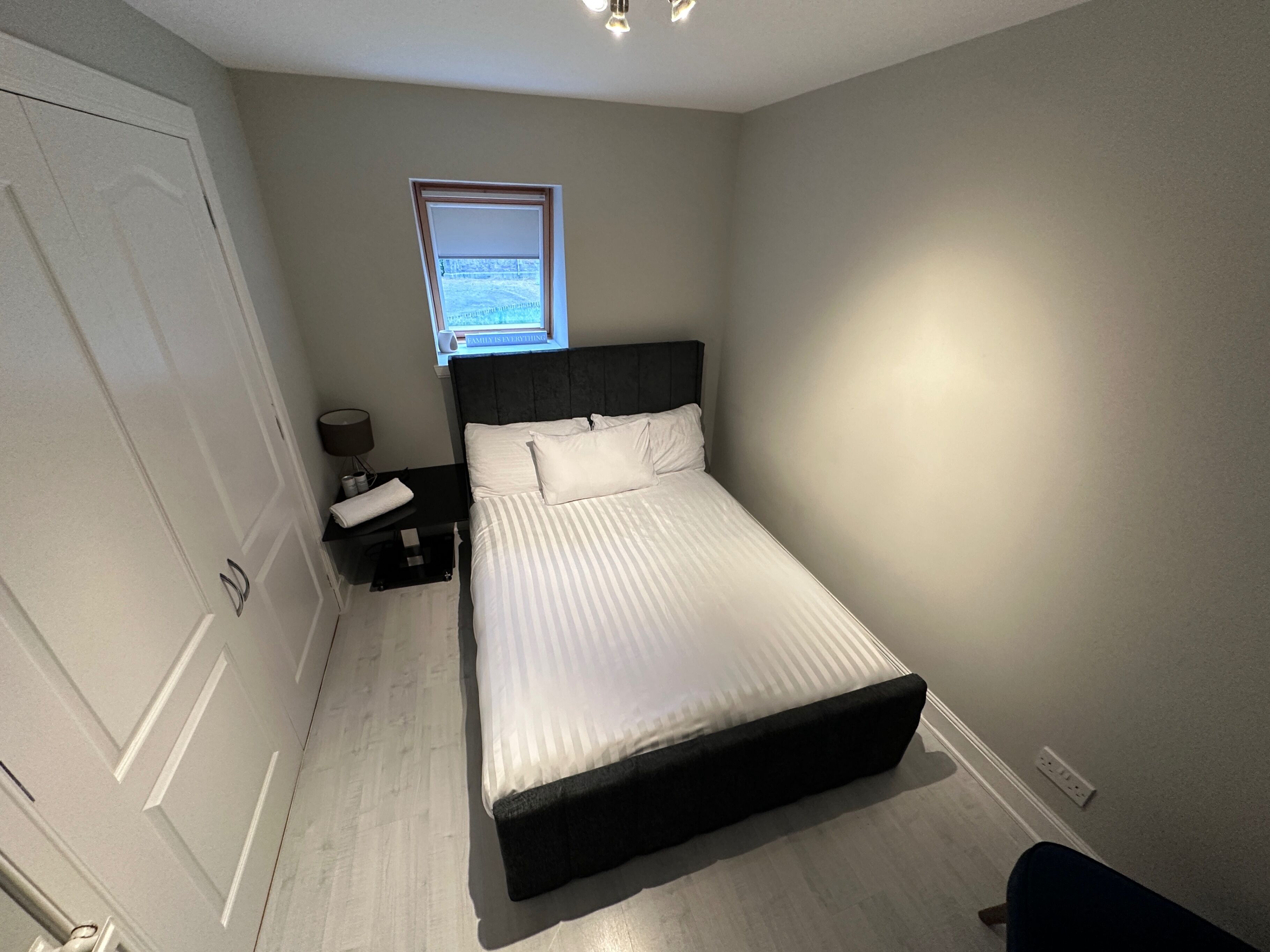 A bedroom with a bed, a nightstand, a lamp, a window, and a door.