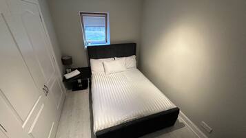 A bedroom with a bed, a nightstand, a lamp, a window, and a door.