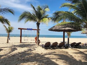 Una playa con un columpio que dice "Ocean Vista", un paraguas de paja y sillas de playa.