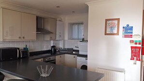 A compact kitchen with white cabinets, a black countertop, a microwave, a kettle, and a washing machine.