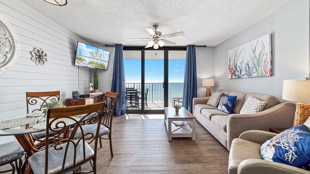 A living room with a balcony, a ceiling fan, a TV, and a view of the ocean. - Sunswept 705  Beach Front - King Bed -  POOL - Orange Beach  (Orange Beach)