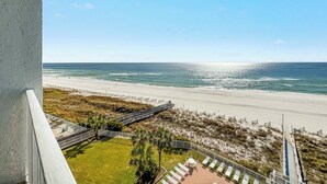 A balcony with a view of a beach, a grassy area with lounge chairs, and a clear sky. - Sunswept 705  Beach Front - King Bed -  POOL - Orange Beach  (Orange Beach)