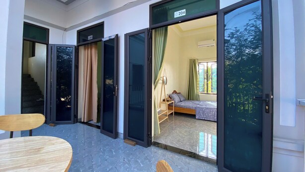 Une chambre d’hôtel avec un lit, une petite table et une chaise. Deux portes-fenêtres coulissantes donnent sur un balcon.