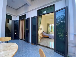 Een hotelkamer met een bed, een tafeltje en een stoel. Er zijn twee schuifpuien die uitkomen op een balkon.