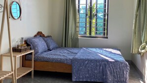 Une chambre à coucher avec un lit, une petite table, un luminaire suspendu et une fenêtre avec des rideaux.