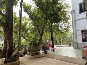 A courtyard with potted plants, a few red chairs, and a white building in the background. - NhaBoong-Homestay Riverside Ninh Binh (Dai Hoang)