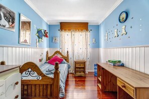 Classic bedroom with a wooden bed, bedside table, and nightstand, featuring a window with a floral curtain.
