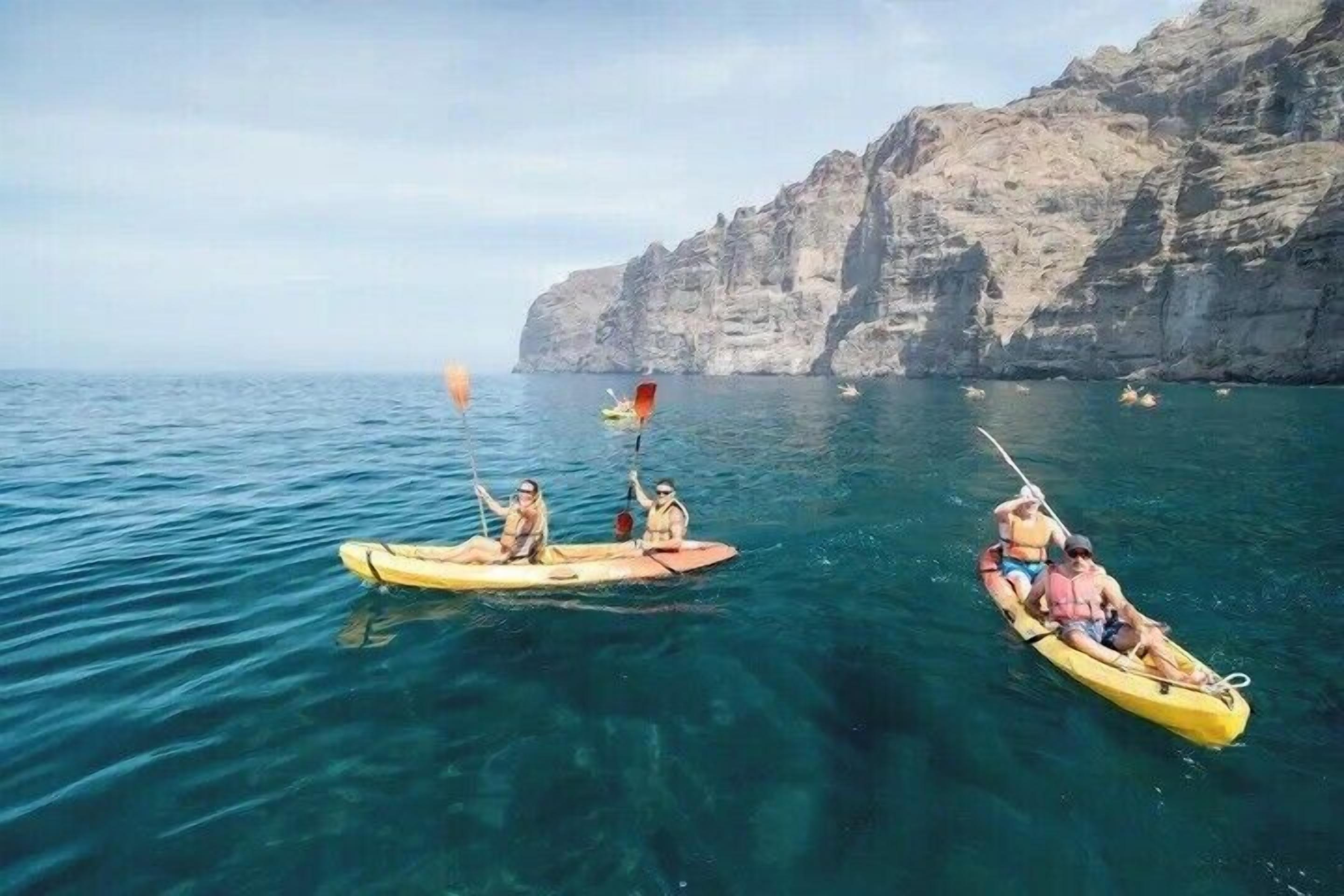 Two kayaks on calm water with a rocky cliff in the background.