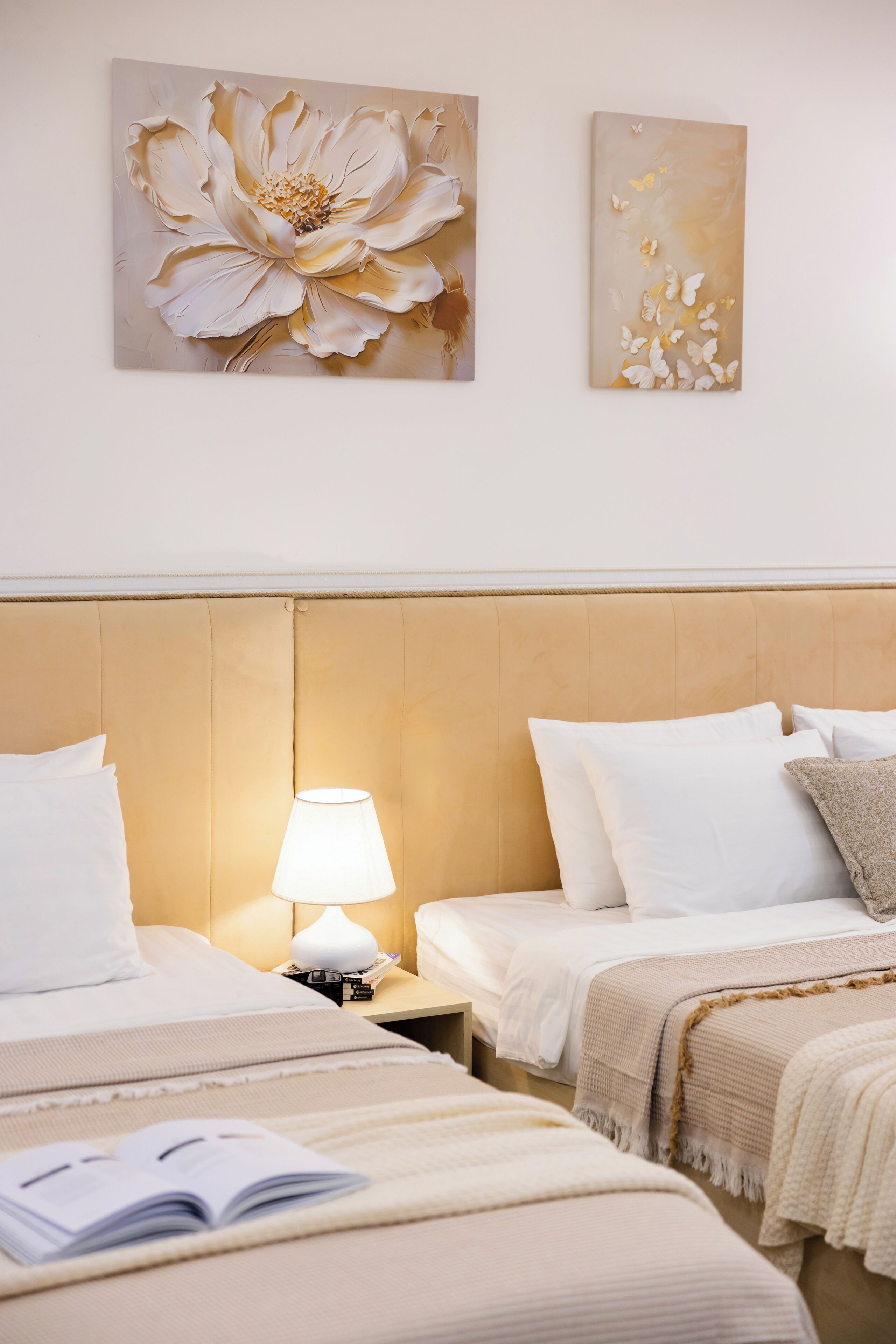 A hotel room with two beds, a nightstand with a lamp, and two wall-mounted artworks.