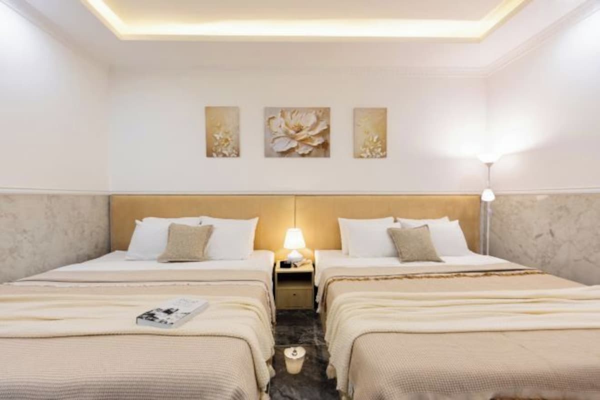 Quarto de hotel com duas camas, uma mesa de cabeceira com abajur e três quadros de flores pendurados na parede.