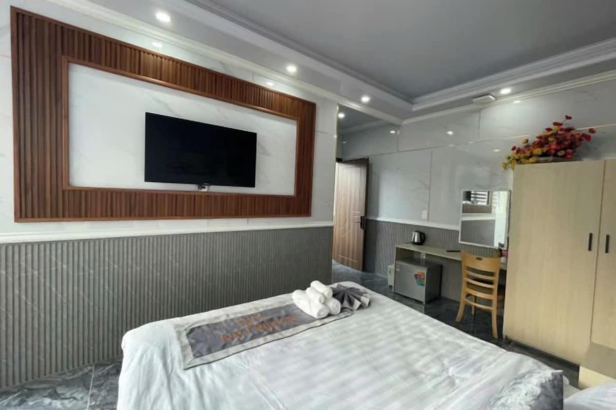 Quarto de hotel moderno com uma cama grande, televisão de tela plana na parede, pequeno espaço de cozinha e um guarda-roupa.
