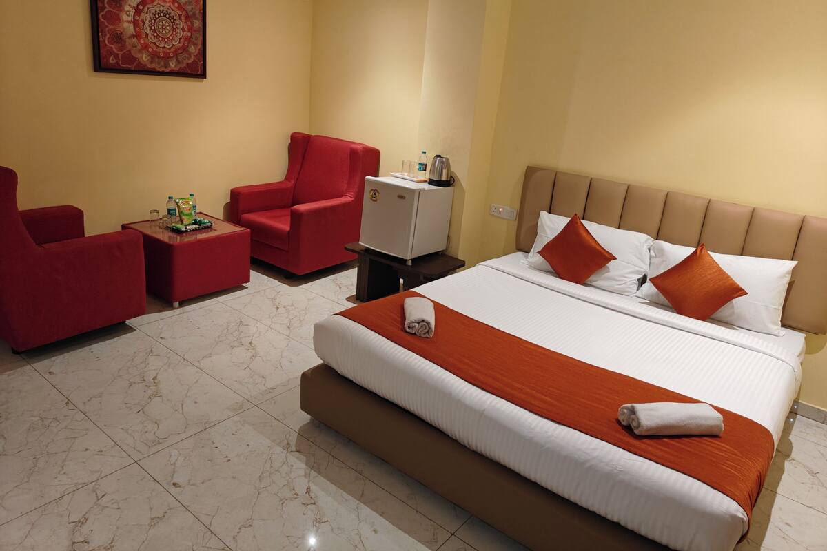 Una habitación de hotel con una cama grande, un sillón rojo, una mesita y un televisor.