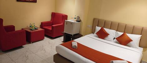 A hotel room with a large bed, a red armchair, a small table, and a television.