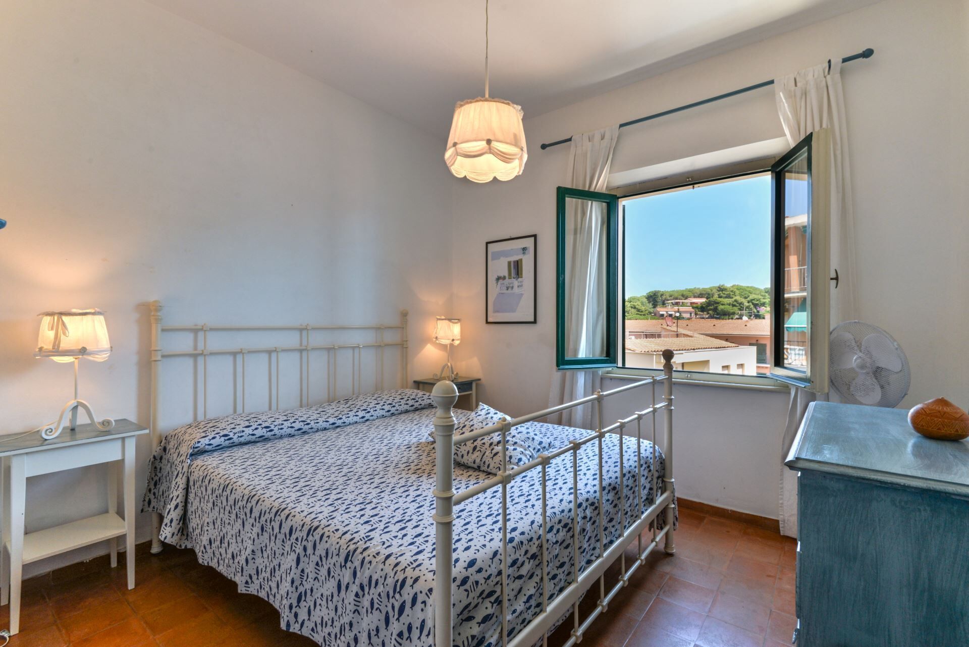 Un dormitorio con cama, lámparas de noche, ventana con vistas y cómoda.