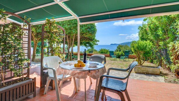 Une terrasse extérieure avec une table et des chaises, une vue sur la mer et une pergola verdoyante.