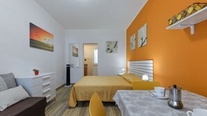 Une chambre d’hôtel avec un lit, un canapé, une table avec une cafetière et des œuvres d’art accrochées aux murs.