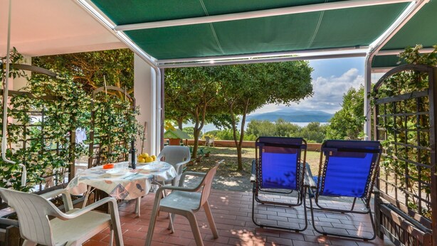 An outdoor patio with a table and chairs, a green canopy, and a view of the landscape. - Residenza - Le Nereidi - Maia (Capoliveri)