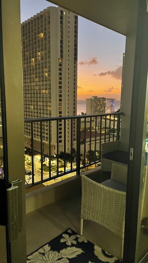A balcony with a view of high-rise buildings and a sunset.