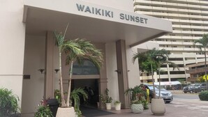 Das Hotel Waikiki Sunset mit überdachter Einfahrt, Palmen und Parkplatz.