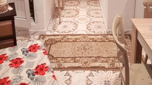 A narrow hallway with a wooden door at the end, a small table with a vase of flowers, and a patterned rug on the floor.